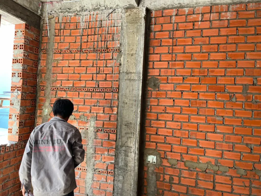 Thợ xây miết mạch vữa và dùng quả dọi kiểm tra độ thẳng của bức tường gạch.